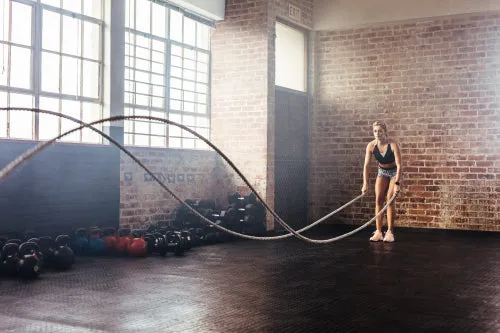 Athlete exercising in gymnasium using training ropes.