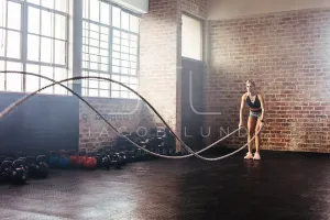 Athlete exercising in gymnasium using training ropes.